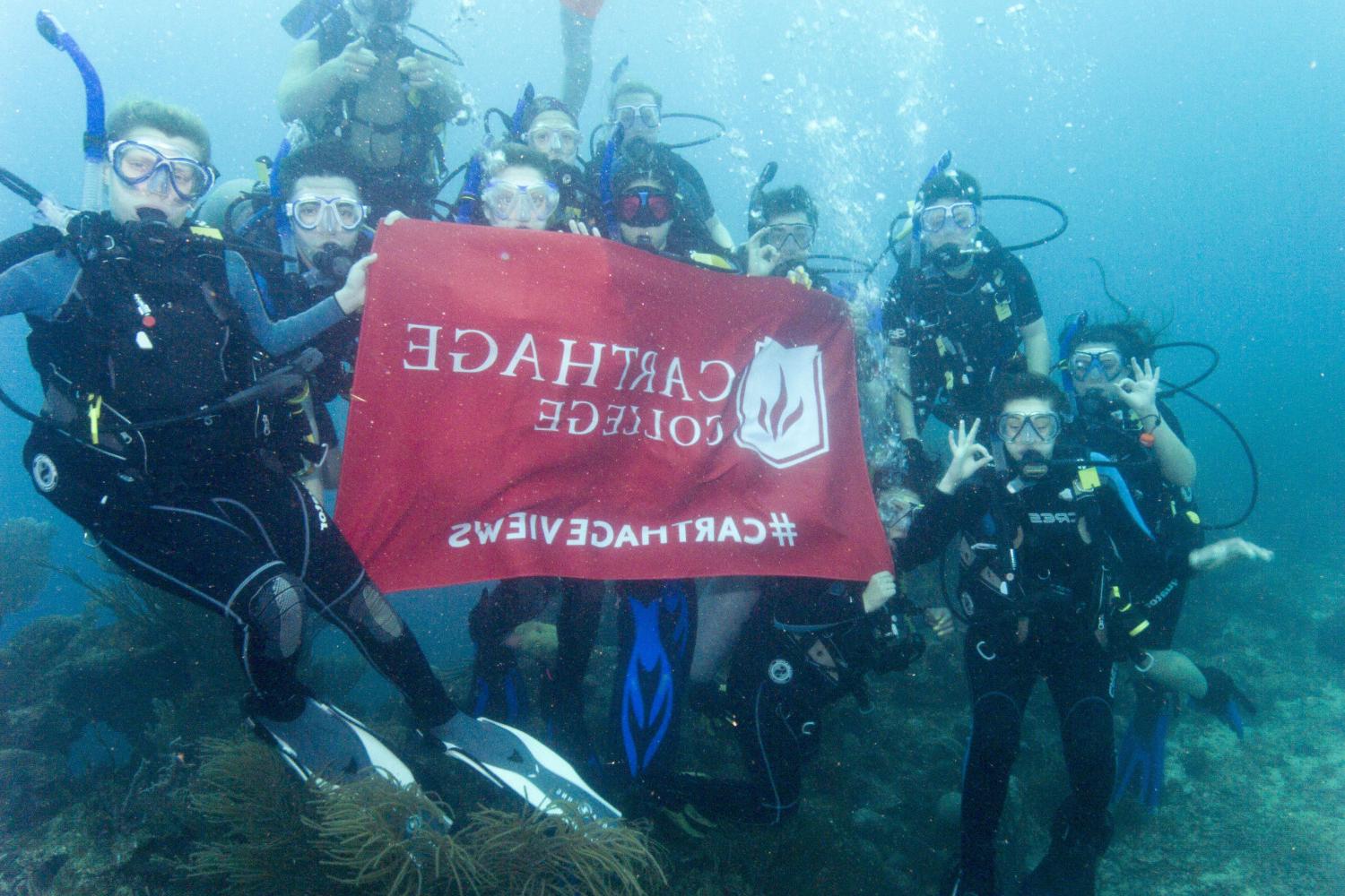 Students hold a Carthage flag while scuba diving on the J-Term study tour to Honduras.